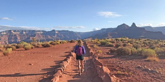 A woman walking along a dirt road towards the mountains