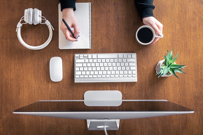 A person at a desk with pen and pad of paper looking at computer.
