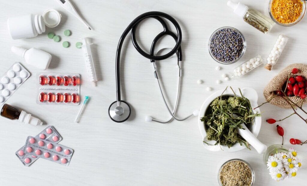 Pills, thermometer, syringe and stethoscope from traditional medicine next to bowl of herbs, flowers and spices from holistic medicine