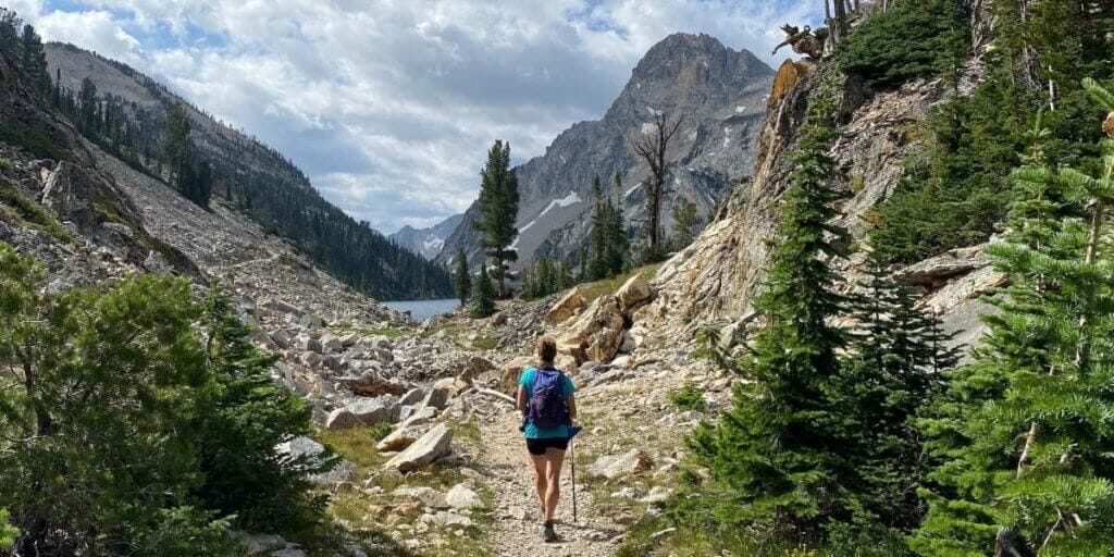 Woman hiking with physical vitality on a path through mountain valley opening up to crystal blue lake