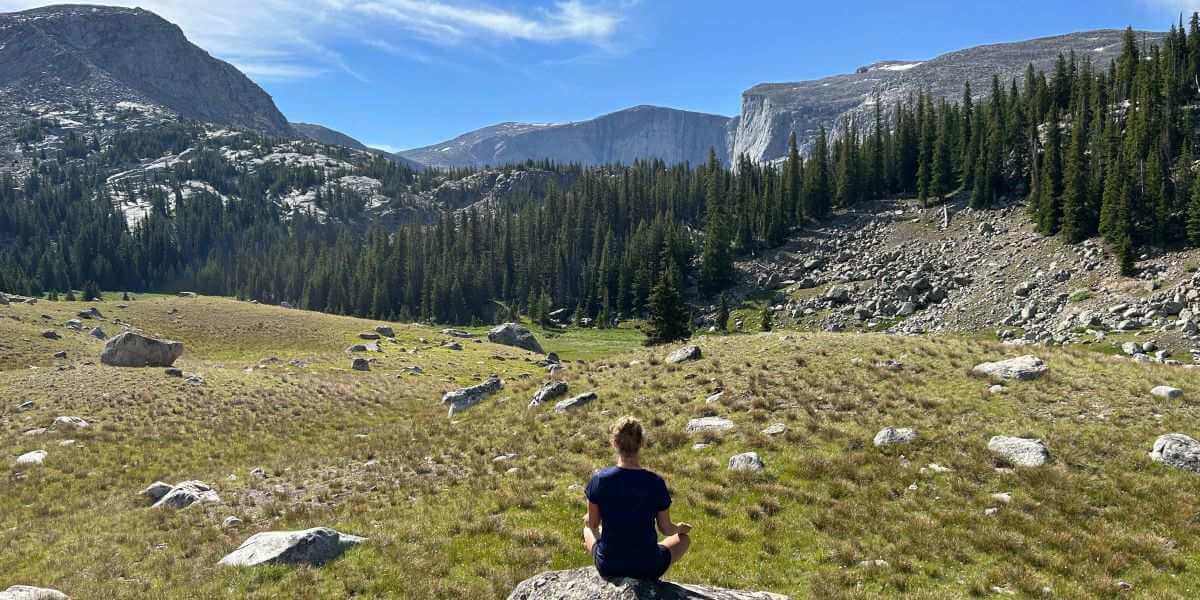 Woman sitting on a rock in a mountain valley meditating to develop mental clarity