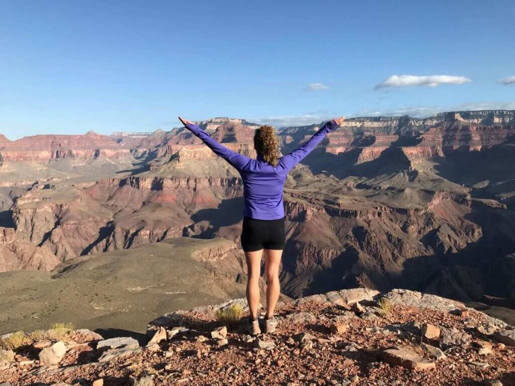 Woman standing at edge of Grand Canyon with arms reaching upwards contemplating life purpose for mental clarity
